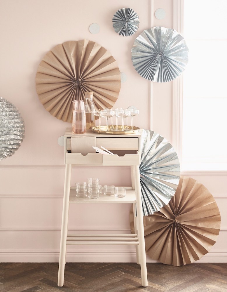 Large silver and brown paper rosettes attached to a light pink wall with a wooded bar cart on a herringbone wood floor