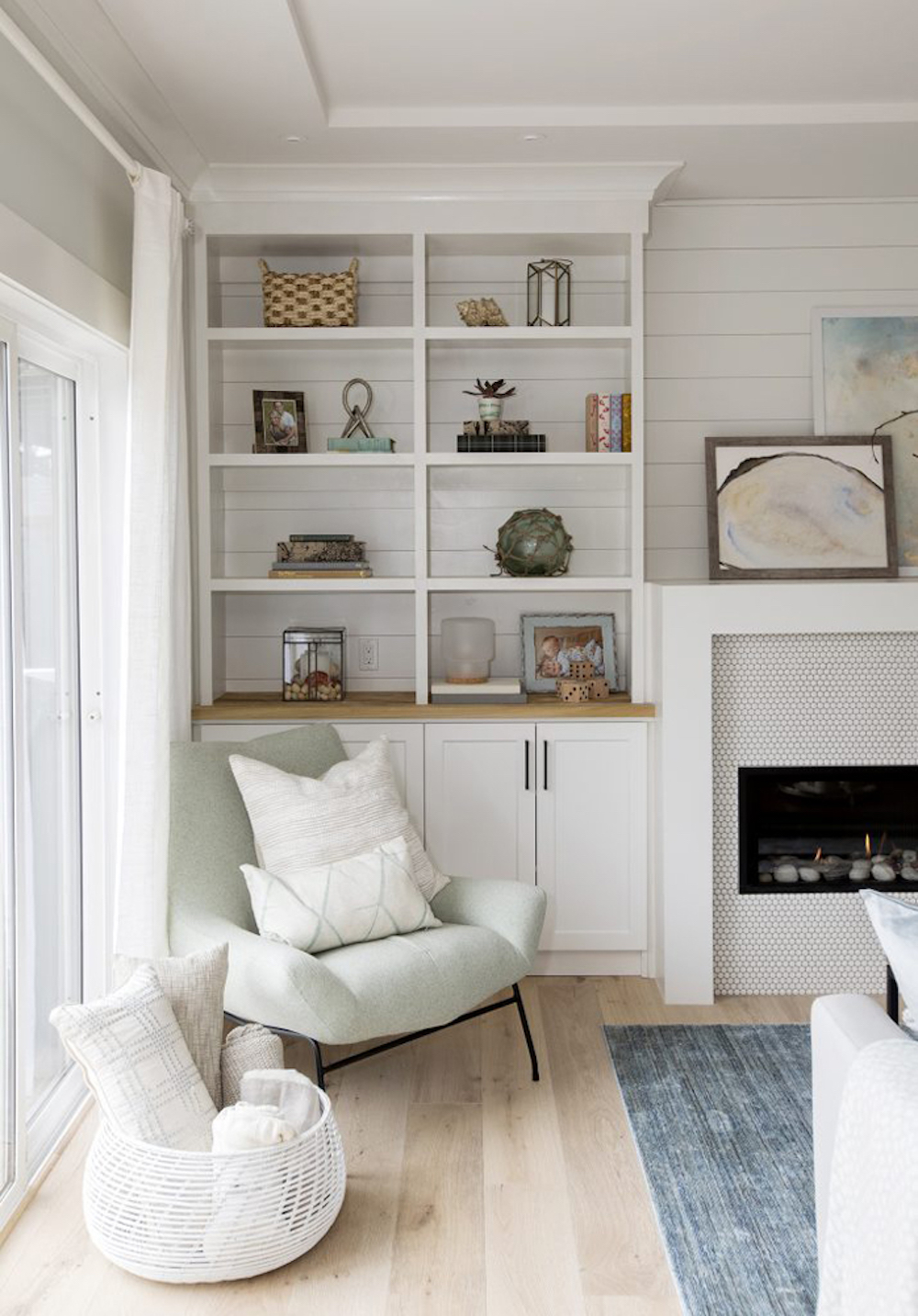 Beautifully curated bookshelves with a selection of photographs, candles, plants, art and mementos on a featured wall in an all-white living room featured on HGTV