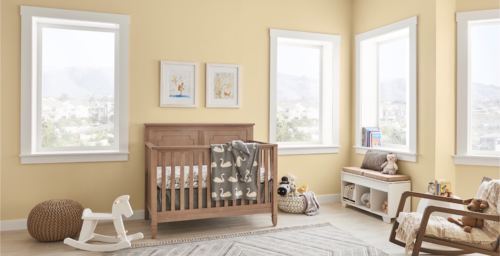 Light and bright nursery with two big windows, a wooden crib, white rocking horse and walls painted in BEHR Pale Honey PPU6-08 + Ultra Pure White 1850