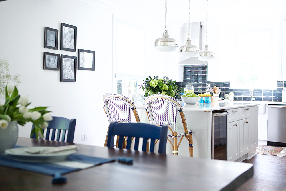 Coastal-inspired kitchen design with white walls, blue subway-tile backsplash and bistro chairs.