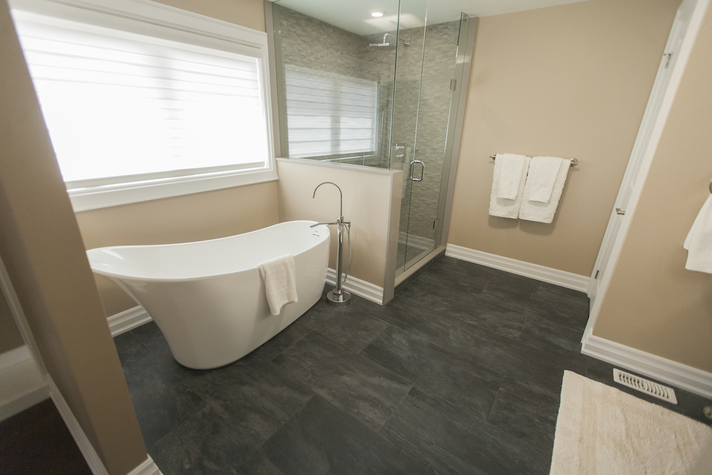 Luxury master bathroom with white soaker tube, large grey tile floors and a walk in shower