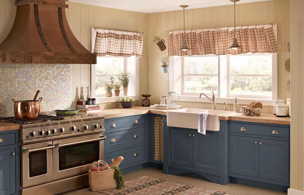 Charming country kitchen with large copper over hood, stainless steel range, pretty red and white curtains, wooden countertops, creamy walls painted in BEHR Raffia Ribbon PPU7-20, and blue cabinets painted in BERH Nypd N480-6