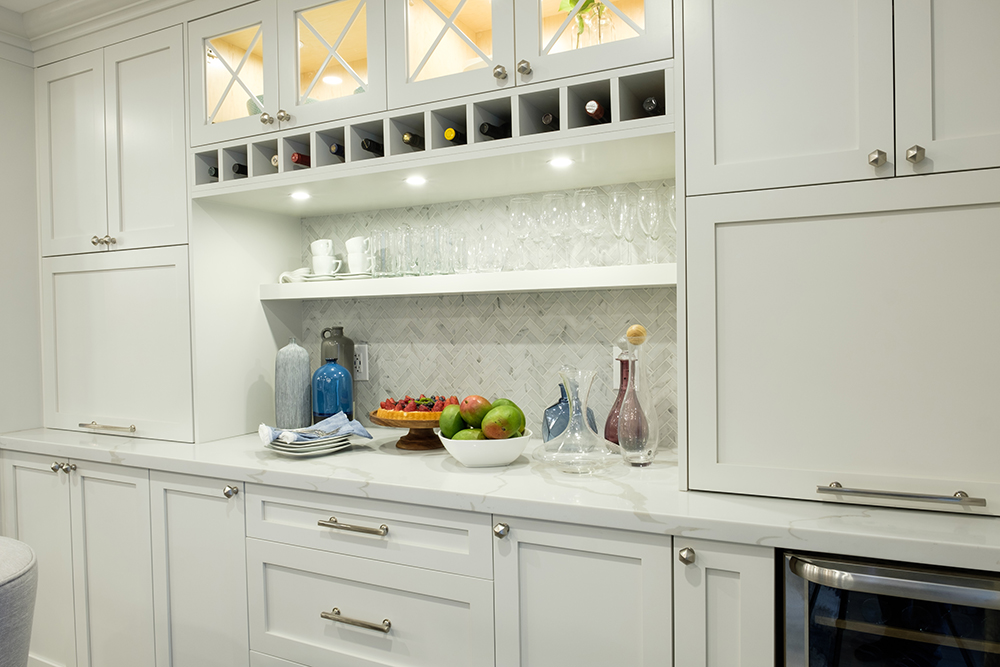 Wall of white cabinets as part of an at home bar area complete with a fridge and wine storage
