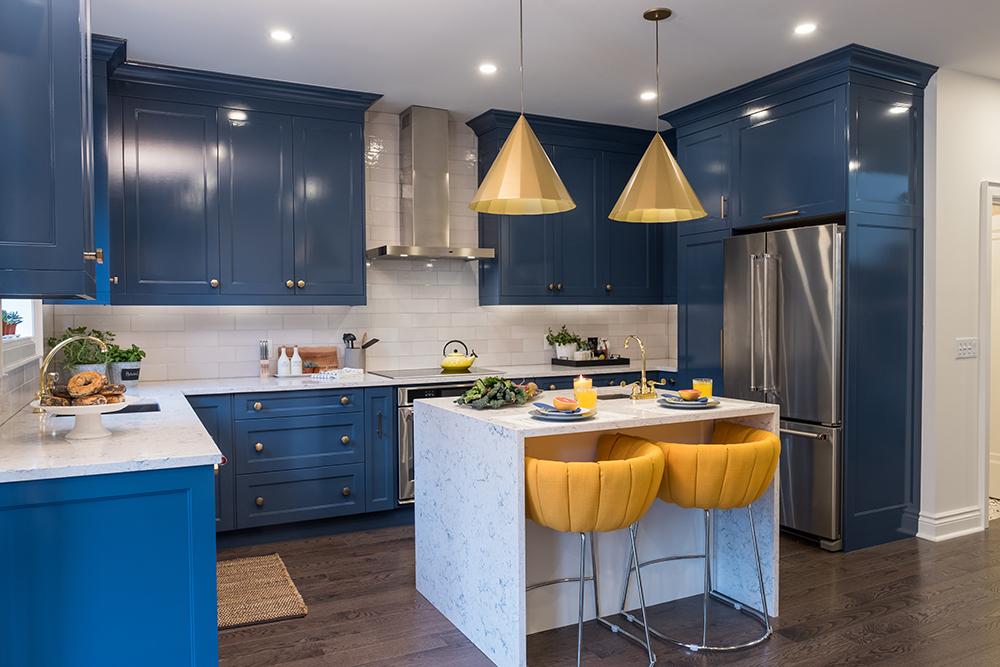 A modern kitchen features blue cabinets, a white quartz breakfast island and gold pendant lights