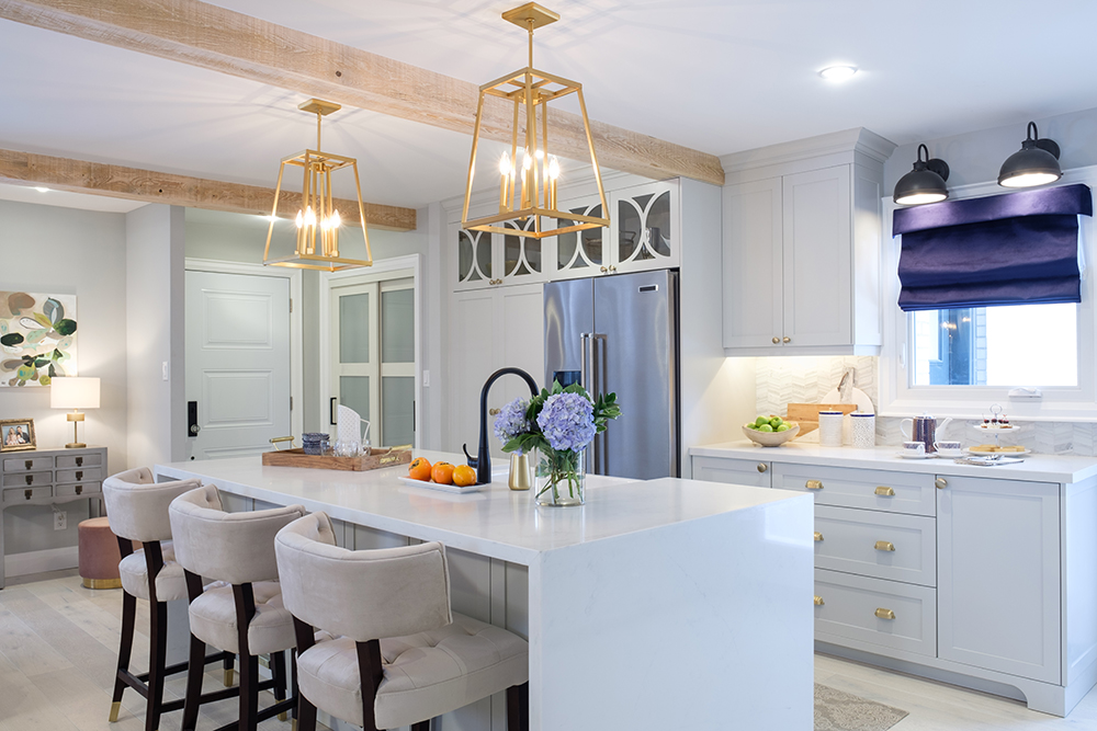 Modern white kitchen with centre island, two gold chandeliers and two wood wrapped beams