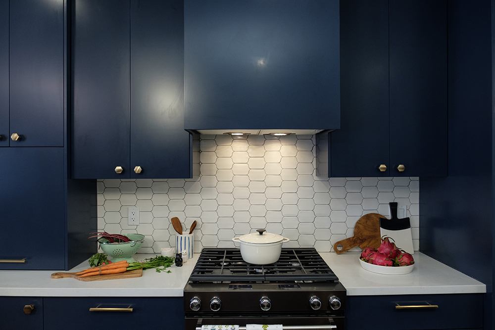 Dark blue cabinets surround a white honeycomb-tile backsplash in a modern kitchen