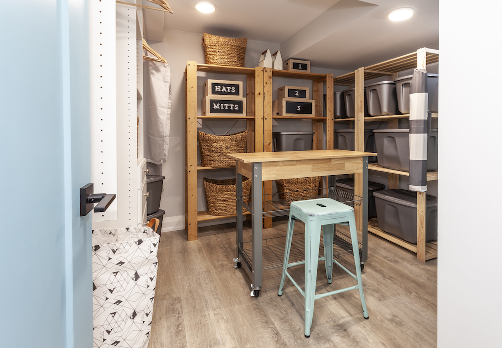 Organized basement storage room filled with wooden shelves, white cabinets, a table on casters and blue stool
