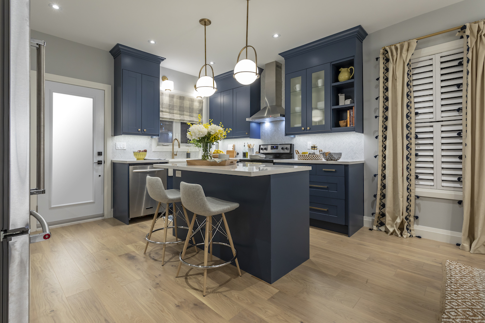 Resprayed blue kitchen cabinets are a feature in this renovated kitchen with white quartz countertops and two grey bar stools