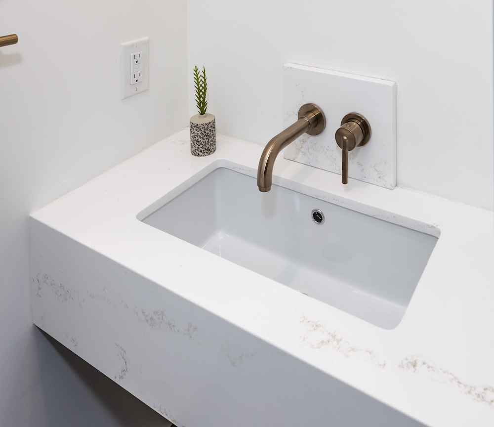 Small quartz covered floating vanity and sink with a bronze faucet in a tiny powder room