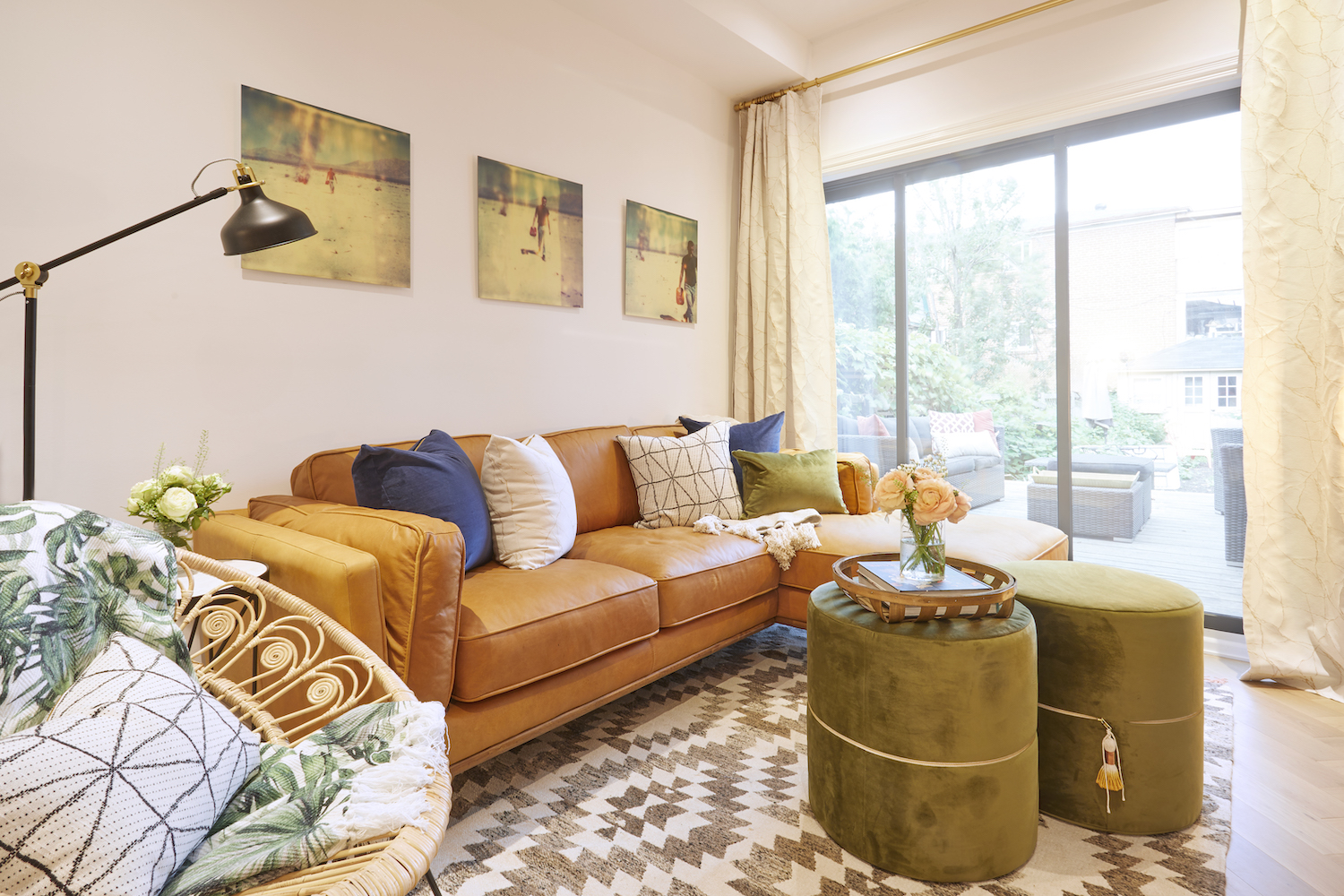 A modern bohemian living room with an orange leather couch, green ottoman stools and a patterned rug
