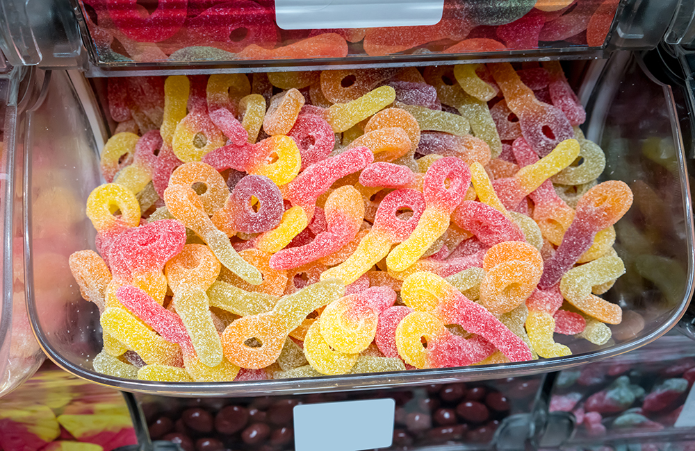 Closed up fizzy and sour gummy jelly in plastic container at confectionery shop.
