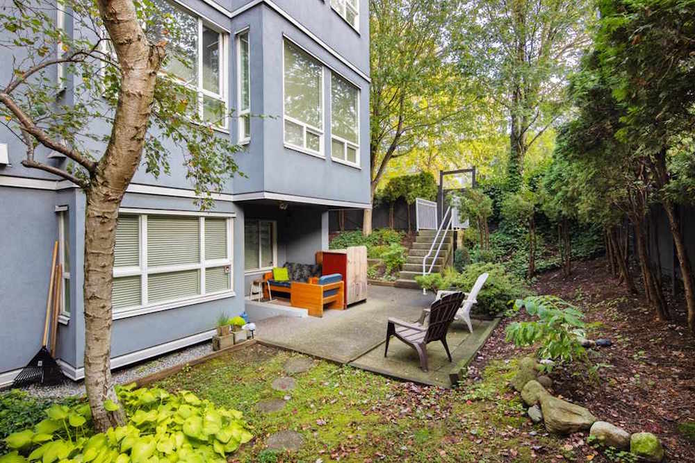 blue condo building with back patio, green trees and bark mulch