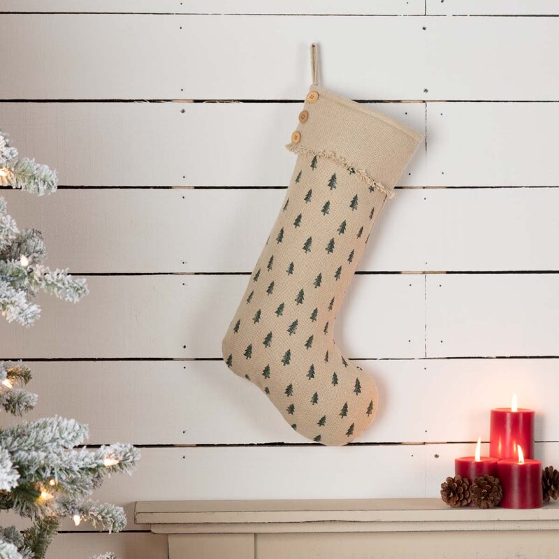Burlap Christmas stocking stamped with green Christmas trees hanging on a white shiplap wall above a mantel with three red candles and pinecones