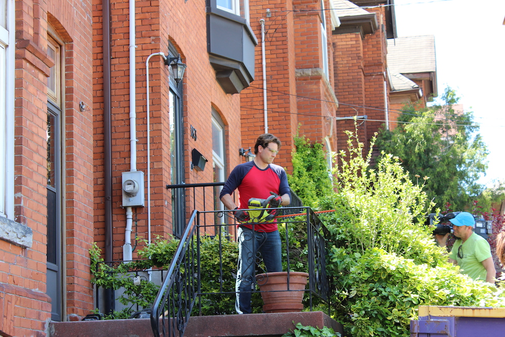 Buyers Bootcamp Victorian character home Scott McGillivray cuts back plants outside a brick house in Hamilton