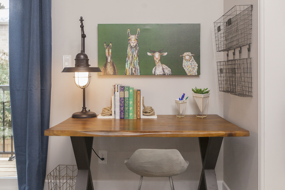 Cute work design with black industrial lamp, books, wire wall organizers and a green painting of farm animals