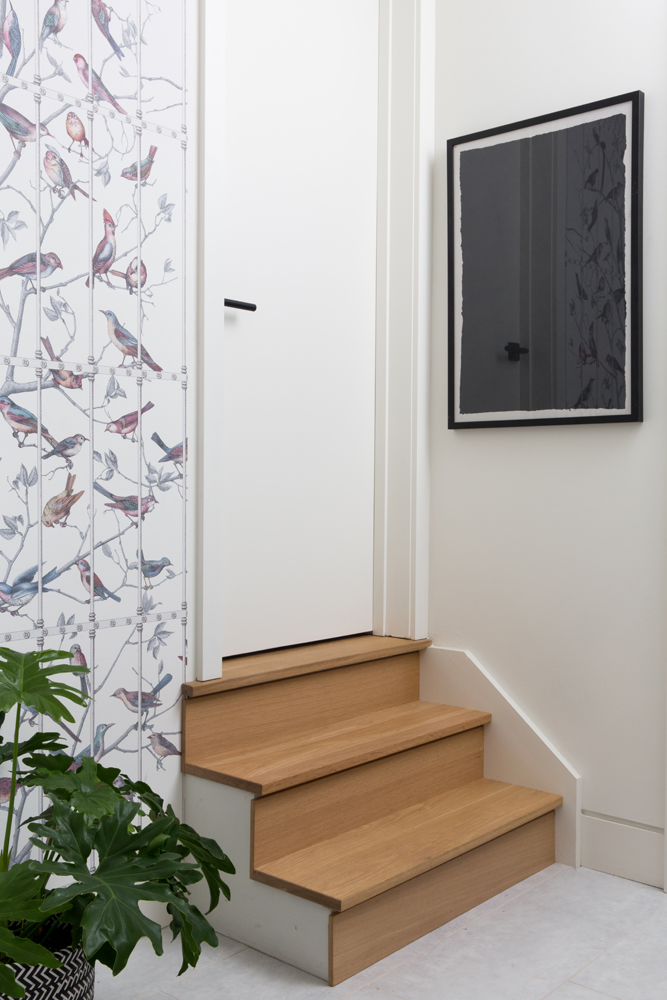 Three wood-tone stairs to white door flanked by wallpaper and black artwork