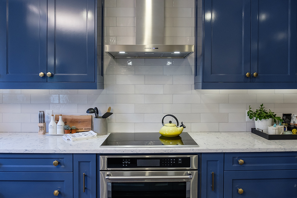 This modern kitchen features blue kitchen cabinets, a white quartz countertop, stainless-steel oven and hood and muted gold hardware