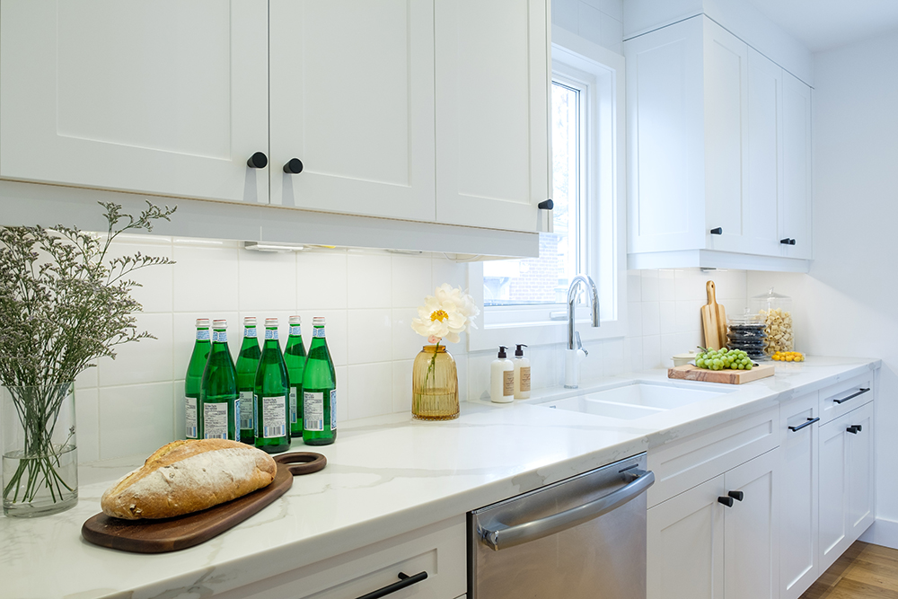 White modern kitchen with quartz countertops, a loaf of bread, bottle of San Pellegrino water and white shaker cabinets