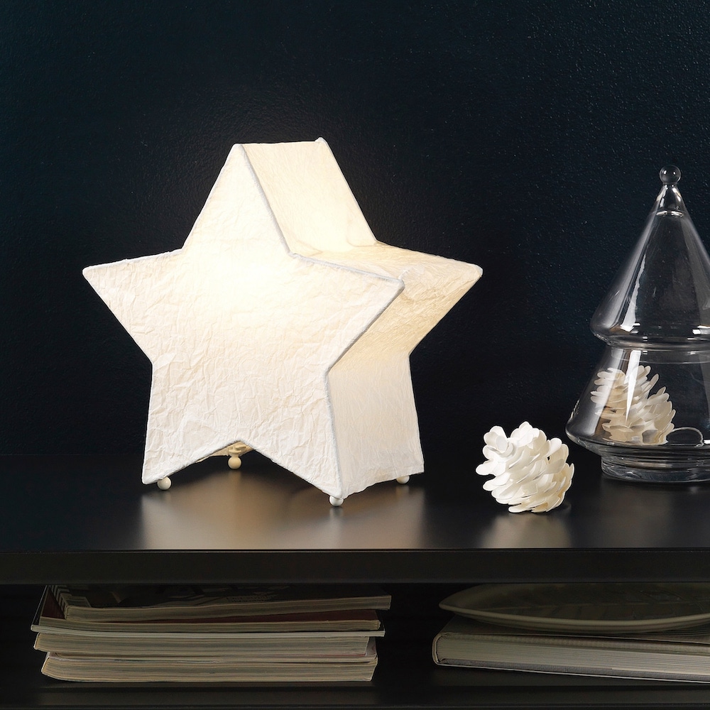 White paper star lamp sitting on a black table with a white paper pinecone and glass Christmas tree ornament