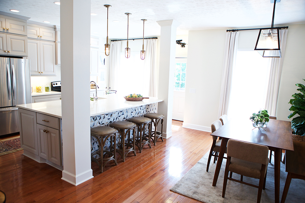 Newly renovate kitchen with two posts, hardwood floors, a massive island, white countertops and four stools