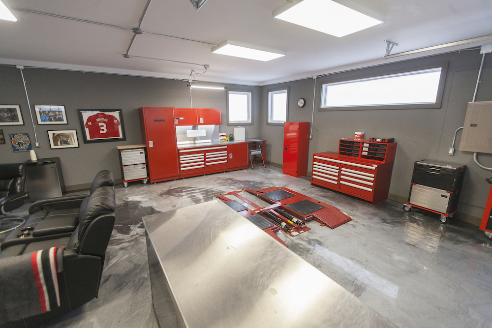 Chic modern garage with single car lift, framed photos on the wall and red car tool cabinets