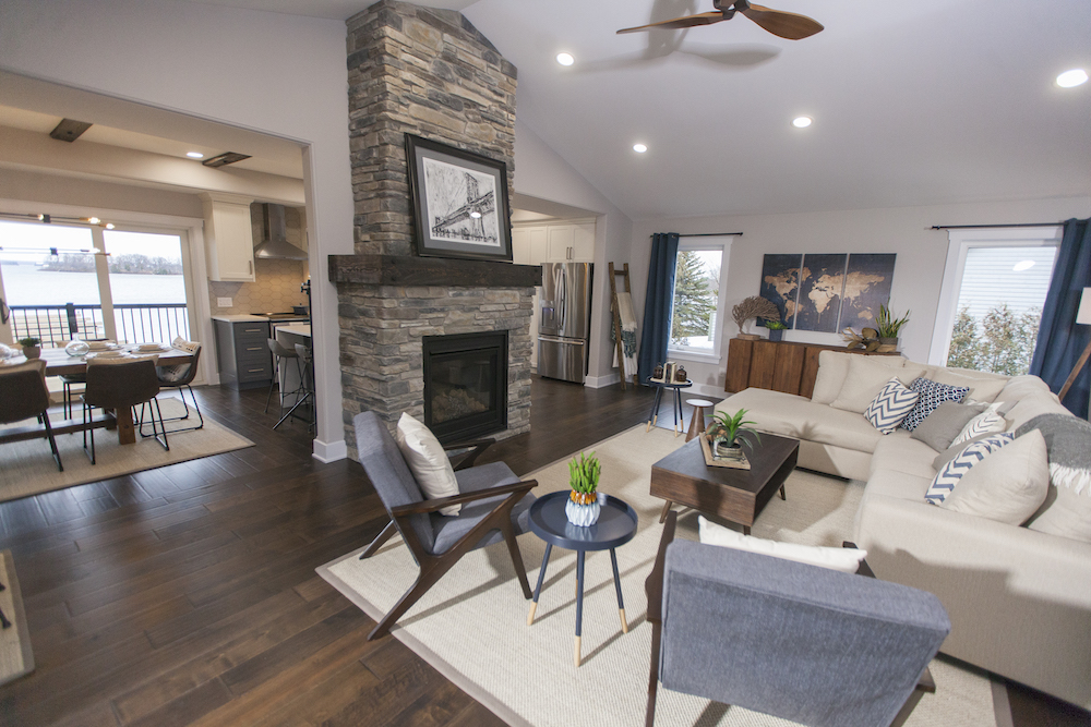 Modern open concept living room with a stone fireplace, blue armchairs and large white couch