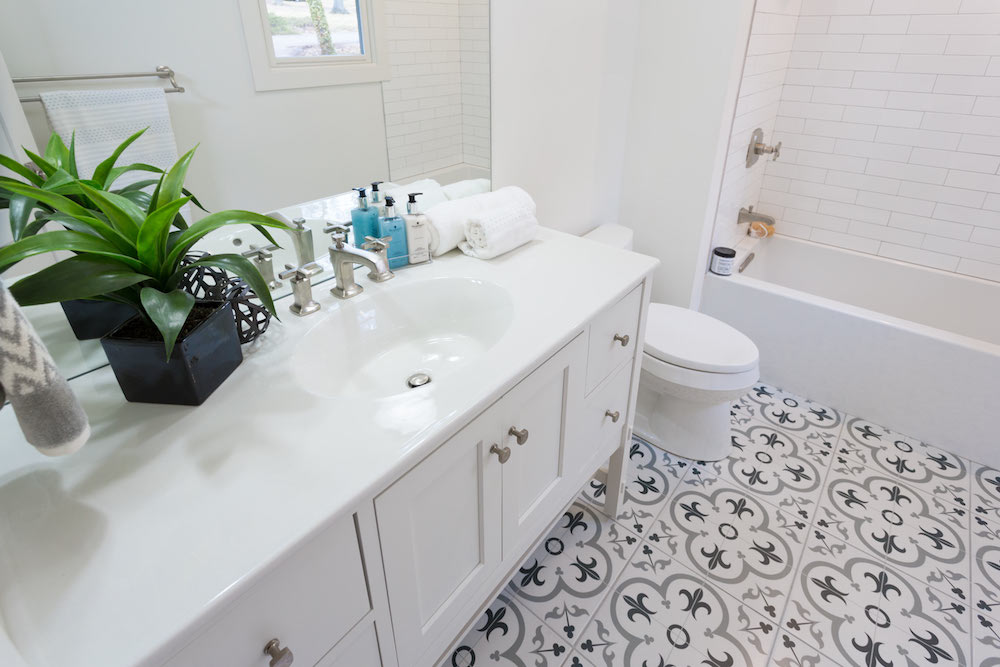 Masters of Flip split level guest suite ensuite bathroom with white sink, vanity and bathtub and geometric grey and white fleur-de-lis floor tiles