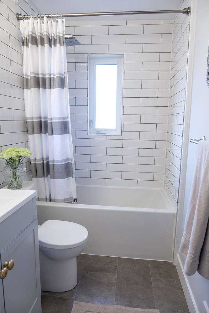 Modern white bathroom with large grey floor tiles, underfloor heating, white tub and striped shower curtain