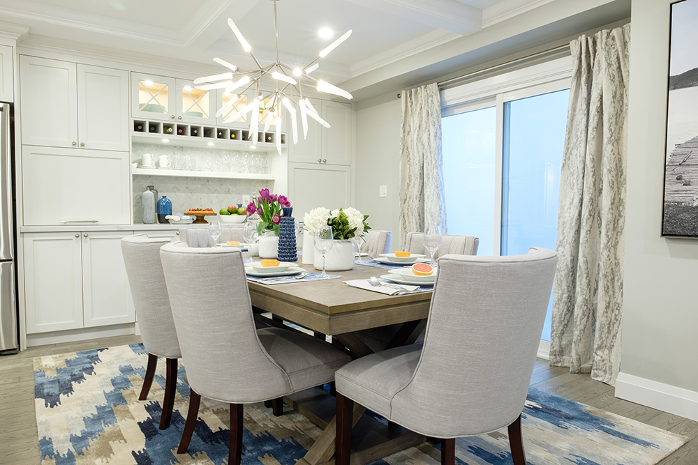 A modern chandelier hangs above a chic modern dining table sitting in front of glass sliding doors