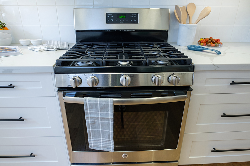Stainless steel gas range flanked by white quartz countertops and white shaker cabinets with black metal pulls