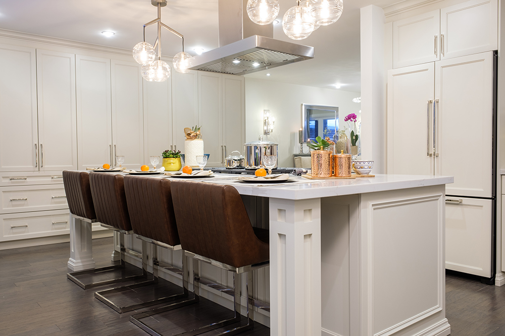 An oversized kitchen island with four brown leather sit up stools in a chic white kitchen