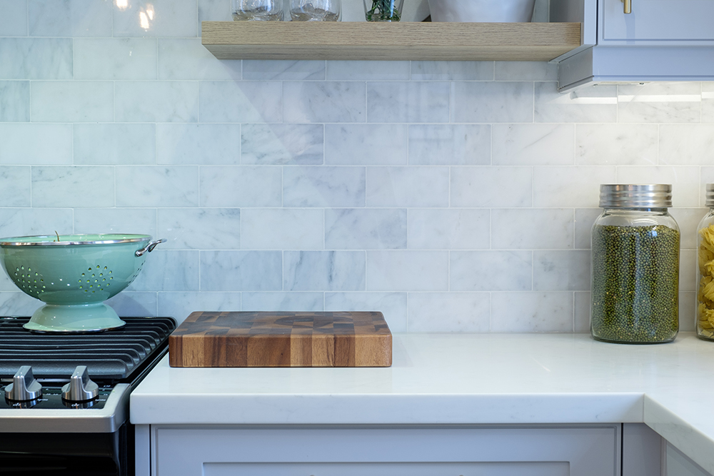 A kitchen backsplash of white and grey-veined stone subway tile and wood butchers block on a white counter
