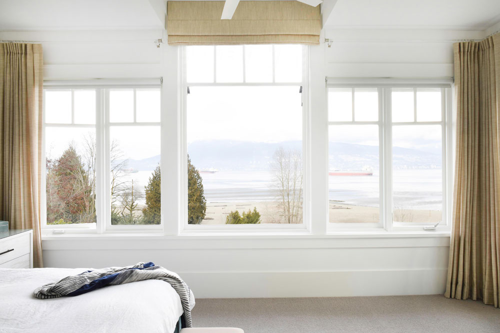white bedroom windows with beige roman blind in center and beige drapes