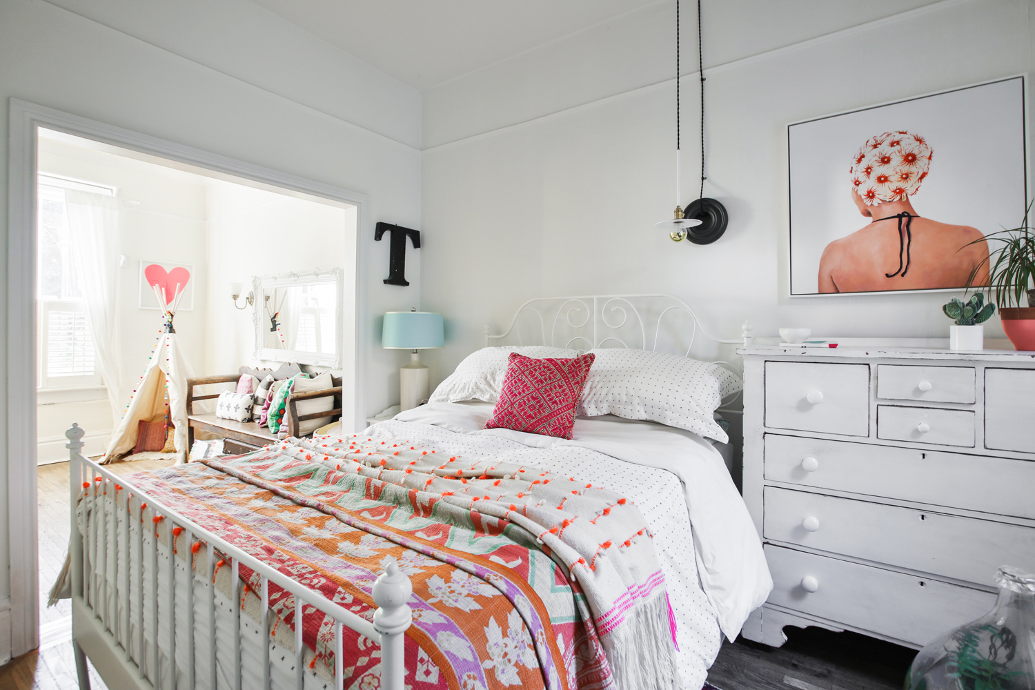 Master bedroom with pink and orange throw and vintage white dresser