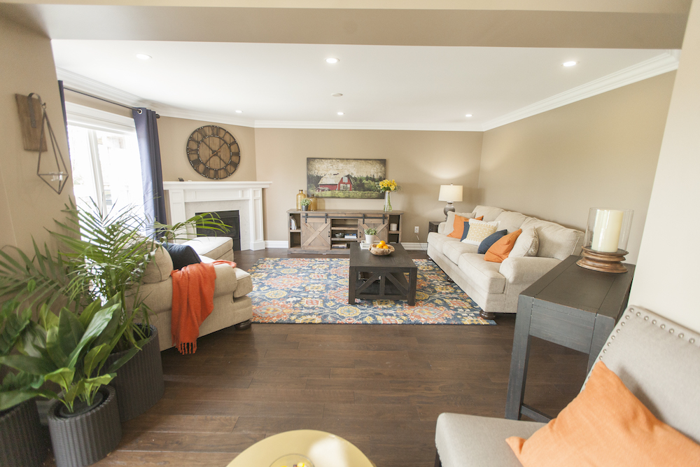 Bright family room with large multicoloured carpet, beige furnishings and large clock above a gas firepalce