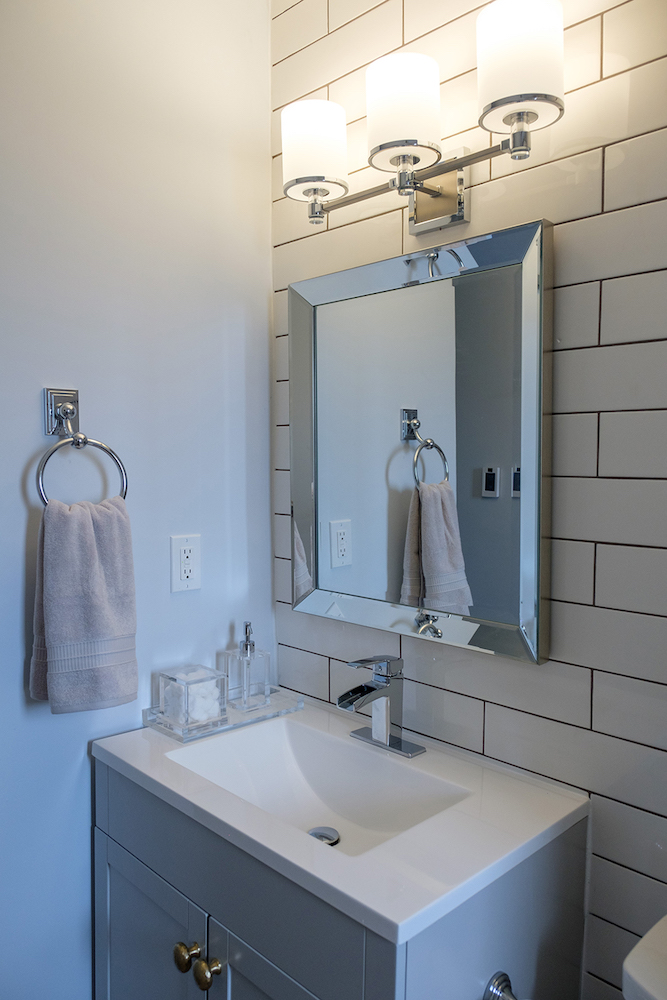 Modern bathroom vanity with a white top and grey cupboards and a subway tile backsplash