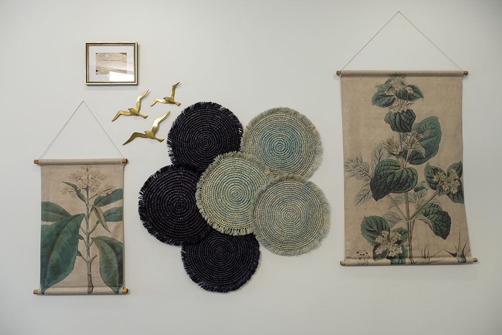 A textural feature wall with a three gold birds, six black and green straw matts and two cloth scrolls with plant designs