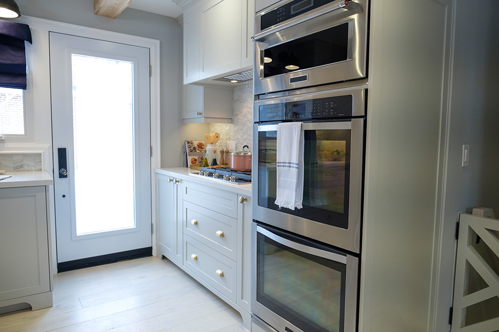 Modern white kitchen with separate gas stovetop and a stack of three ovens