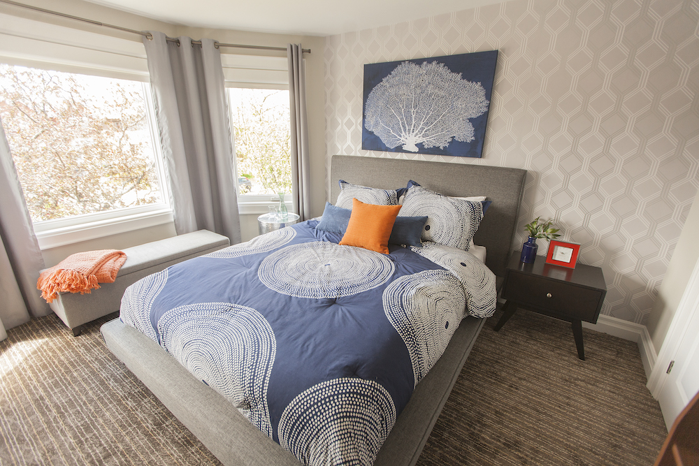 Beautiful bedroom with a grey upholstered bed covered in a blue geometric patterned comforter and an orange pillow