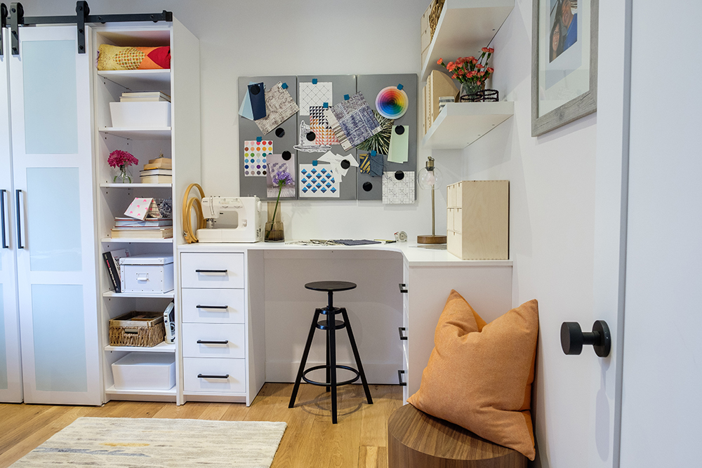 Crafting room with white shelving and desk, black industrial style stool and an orange pillow