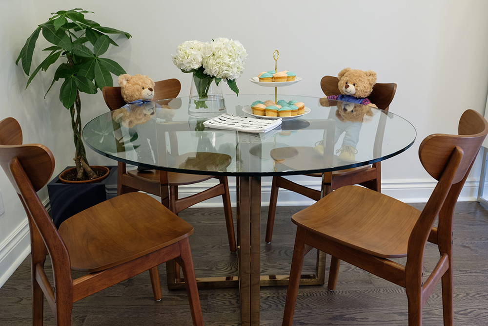 Glass topped breakfast table with four wooden mid-century modern chairs and two teddy bears