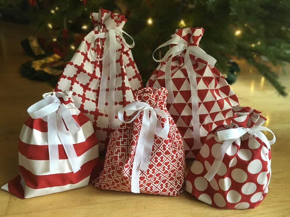 A set of five red and white reusable holiday gift bags sitting under a Christmas tree