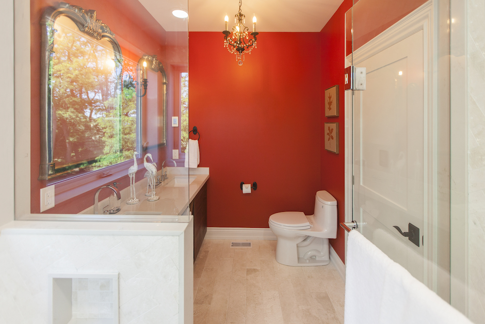 Modern bathroom with red walls, two ornate mirrors and a toilet