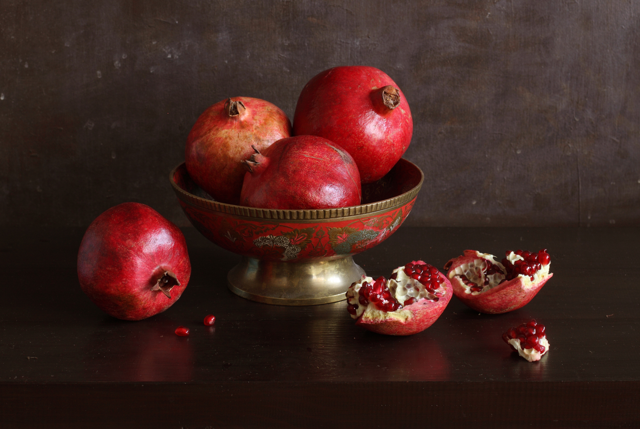 A gold and red bowl filled with pomegranates on a black background