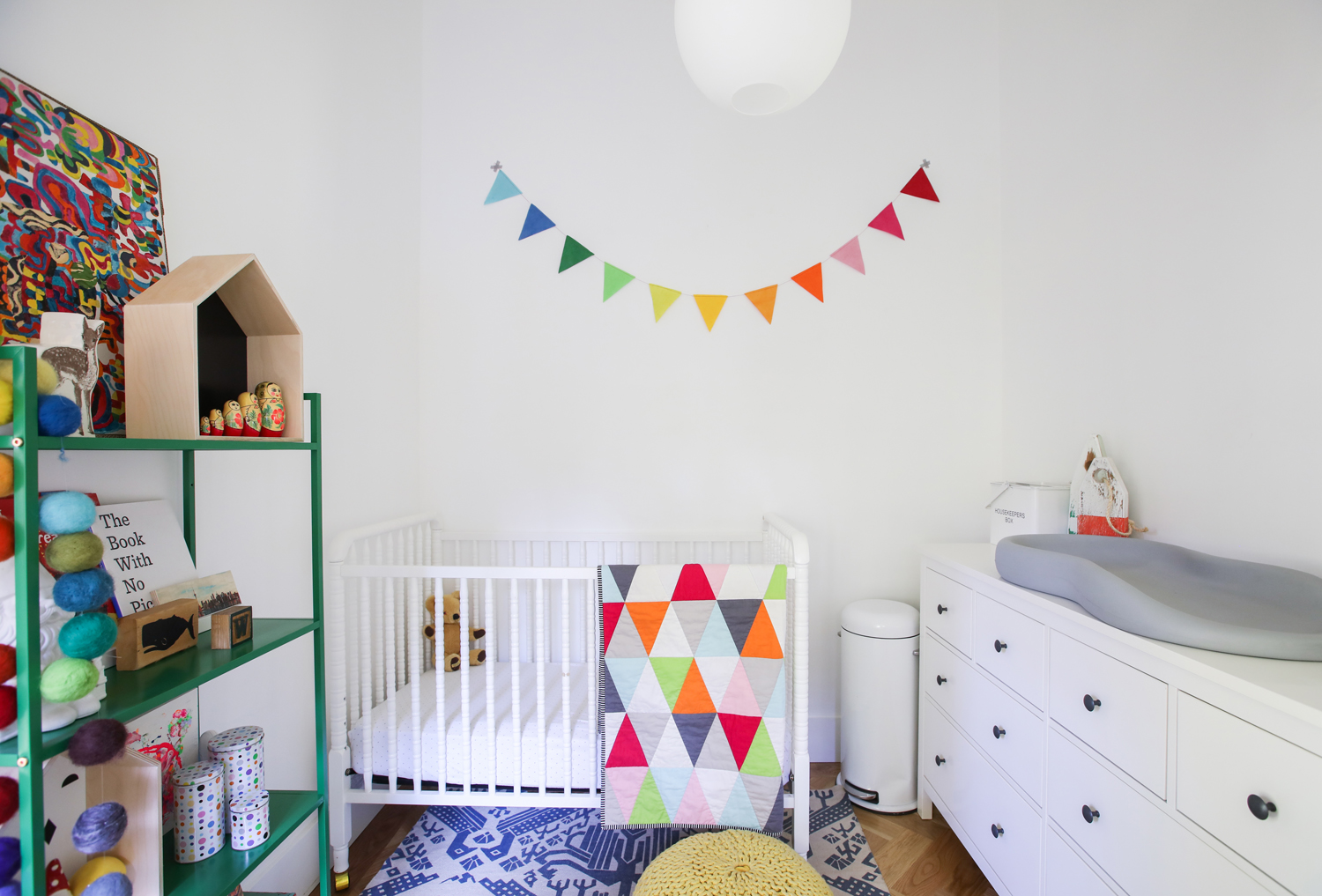 White crib and dresser with rainbow bunting hanging on wall
