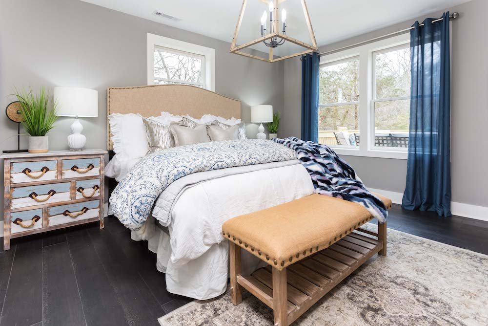Masters of Flip split level master bedroom bed with a pile blue and white quilts, silver throw pillows and beige headboard