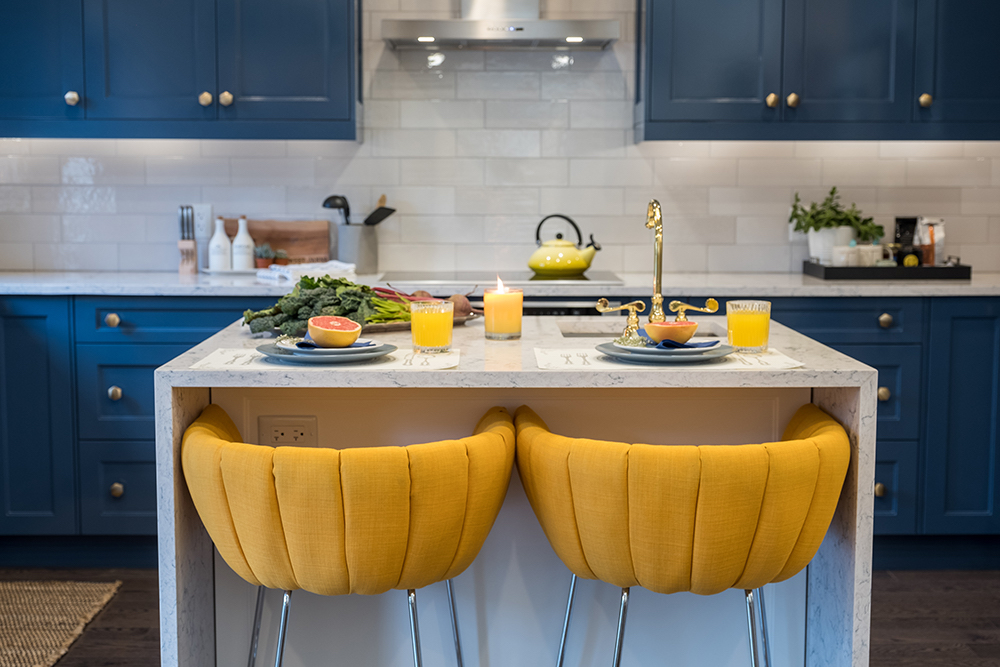 Two vibrant yellow stools tuck in under a white quartz kitchen island set with halved grapefruit