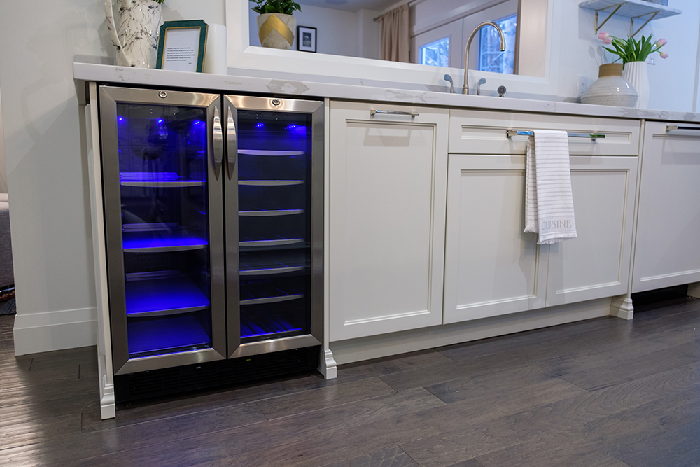 A blue backlit bar fridge in a modern white kitchen surrounded by white cabinets