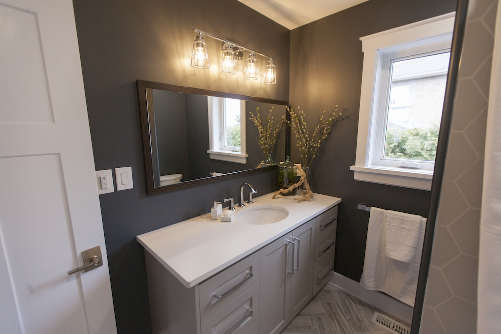 Chic modern bathroom with grey herringbone tile floors, large grey vanity, rectangular mirror and dark grey walls