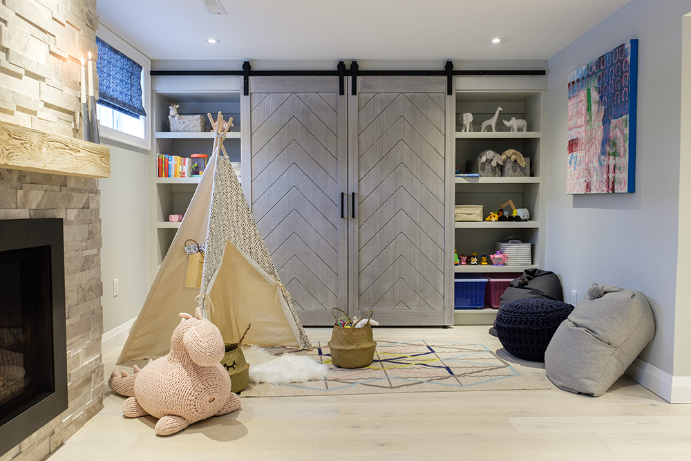 Stylish family room with gas fireplace, pink stuffed horse, a play teepee, grey barn doors and multiple poufs